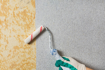 Pasting an old wall with grey wallpaper. The craftsman compacts the wallpaper pasted to the wall with a roller. Apartment renovation