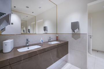 A stylish restroom showcases two elegant sinks with modern faucets, large mirrors, and minimalist decor. The clean lines and neutral colors create a calming atmosphere