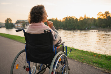 Wall Mural - Sad senior woman sitting in wheelchair walking on road in city outdoor, back view. Old paralyzed lady in chair for people with disability feel depressed. Lonely elderly sick woman sits on wheelchair