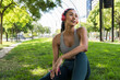 © BUDDHA - Latin sportswoman relaxing on grass wearing headphones in city park