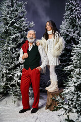 Wall Mural - A joyful man and woman stand amidst snow covered trees, celebrating the festive season together.