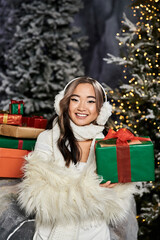 Wall Mural - A person in winter attire holds a gift surrounded by a decorated Christmas tree and presents.