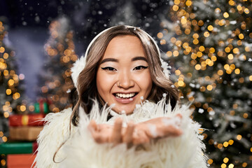 Wall Mural - A cheerful woman in a fluffy outfit delights in falling snow while festive decorations sparkle.