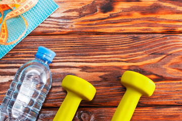 Two yellow dumbbells, a water bottle, and a measuring tape are on a table