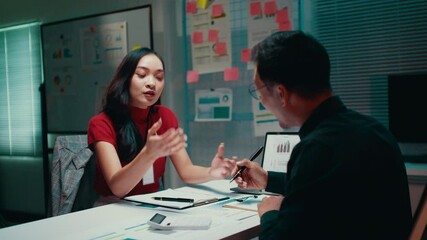 Poster - Asian businesswoman shows a document to her male colleague while seated at a table in a meeting room, engaging in a productive discussion about their project