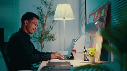 Poster - Asian designer is working late at night in his home office, using a tablet with a pen display. He is smiling and seems to be enjoying his work