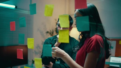 Poster - Business people engage in discussions and strategy planning using sticky notes on a glass wall in an office setting at night, fostering teamwork and collaboration