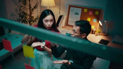 Poster - Two business partners are having a discussion in their office at night. They are using sticky notes on a glass wall to brainstorm ideas