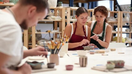 Wall Mural - During master class, student paints clay vessel under guidance of female teacher. Mentor is next to student, makes comments and corrects inaccuracies