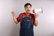 © ArvStd - Young asian man barista barman employee wear blue apron work in coffee shop hold a megaphone while pointing above