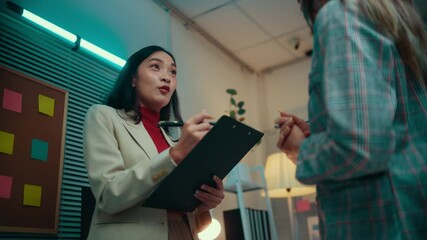 Aufkleber - Businesswoman holding a clipboard and pen engages in conversation with a colleague in a modern office setting, using gestures to emphasize points during their discussion