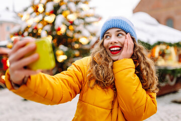 Happy woman wear winter season clothes taking selfie xmas market urban city street. Christmas, new year, Holidays, rest, blogging.