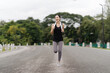 © Wicitr - Determined Runner: A young woman in workout attire runs confidently along a paved road, radiating determination and vitality.  The lush greenery in the background creates a serene atmosphere.