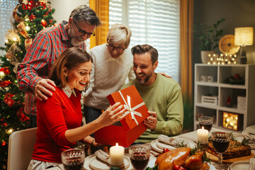 Wall Mural - Family giving christmas gift to surprised mother at dinner table