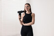 © New Africa - Young woman with percussive massage gun indoors