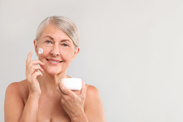 Wall Mural - Senior woman with face cream on light background. Space for text