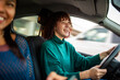 © Paula - Smiling woman driving car with friend in passenger seat
