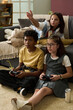 © pressmaster - Group of three friends gathered in cozy living room, engaging in playing video games on separate controllers with focused expressions, showcasing relaxed atmosphere and friendship