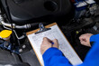 © zphoto83 - Mechanic reviewing maintenance logs while inspecting a vehicle’s engine in an auto workshop during daylight hours