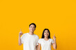© Prostock-studio - Excited asian man and woman pointing upwards at copy space, yellow studio background