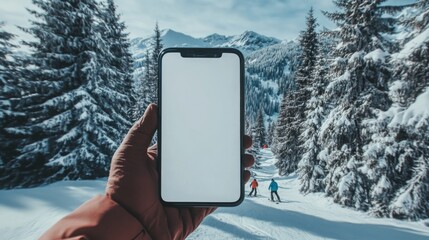Poster - A person is holding a smartphone in their hand with a blank screen. In the background, two skiers are on a snowy slope. The mountains are covered in snow and trees.