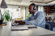 © lordn - Focused man wearing headphones, working on his laptop in a modern, well-lit home office environment.