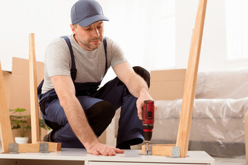 Aufkleber - Handyman Assembling Wooden Table With Electric Drill Sitting On Floor During Renovation Indoor. Carpenter Working Making Desk Furnishing House After Renovation. Carpentry Concept