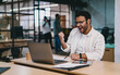 © BullRun - Joyful man celebrating success while sitting at table with laptop