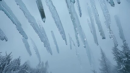 Aufkleber - Surreal sequence of icicles falling from a roof in a snowy landscape. The camera captures the falling ice against a backdrop of snow covered trees and a cloudy sky