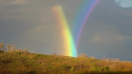 Poster - Bright rainbow is moving across a hilltop with a cloudy sky in the background. The rainbow's movement creates a surreal and mesmerizing effect