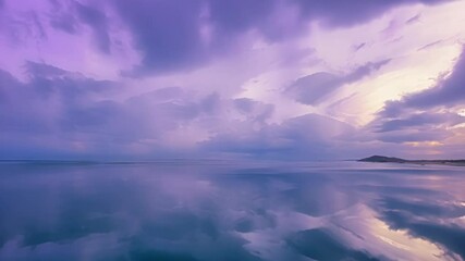 Poster - Purple and orange sky with clouds reflects on the tranquil surface of a water expanse. A small hill rises on the right, enhancing the serene landscape at dusk
