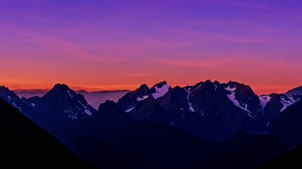 Aufkleber - Mountain range is illuminated by the setting sun. The colors of the sky and mountains gradually shift from warm oranges and yellows to cool purples and blues