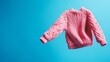 © InfiniteStudio - A pink knitted sweater floats effortlessly against a vivid blue background, showcasing its cozy texture and playful design