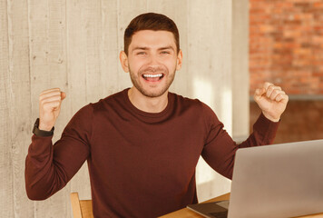 Poster - Business Success. Happy Man Shaking Fists Sitting At Laptop Celebrating Promotion In Modern Office. Selective Focus