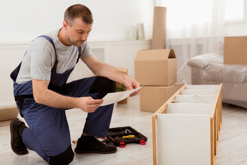 Aufkleber - Male Worker Reading Instruction Installing Wooden Shelf During Renovation Indoors. Professional Handyman In Blue Coverall Uniform Assembling Furniture Kit With Manual. Home Furnishing Service