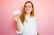 © AntonioDiaz - Portrait of a smiling young woman holding a credit card against a pink background