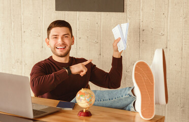 Poster - Upcoming Vacation. Joyful Office Worker Showing Flight Tickets Sitting With Legs On Desk At Workplace Indoor