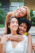© Jose Calsina - Vertical. Three young women smiling and embracing outdoors, enjoying friendship and happiness together, posing cheerfully looking at camera and expressing joy, bonding, and diverse friendship