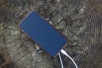 A portable charger charges the smartphone. Power Bank with cable against the background of wood