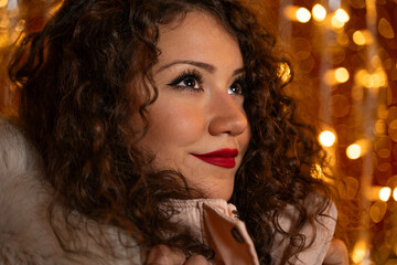 Closeup shot of gorgeous curly hair girl in winter jacket with Christmas lights in back 