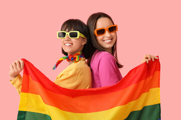 Wall Mural - Young lesbian couple in sunglasses with LGBT flag on pink background