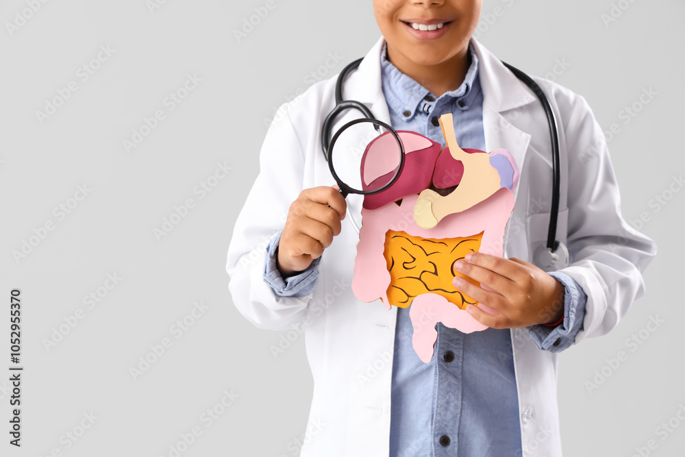 Little doctor with paper digestive system and magnifier on light background, closeup