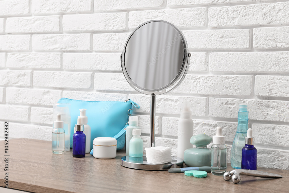 Different cosmetic products, accessories, bag and mirror on table near light brick wall