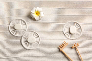 Stones, small rakes and tropical flower on light sand with lines. Zen concept