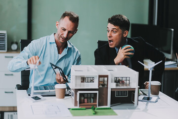 Engineers meeting about wind turbine model and house model. Renewable energy and housing development concept. Team of architects and engineers in modern office discussing design structure.