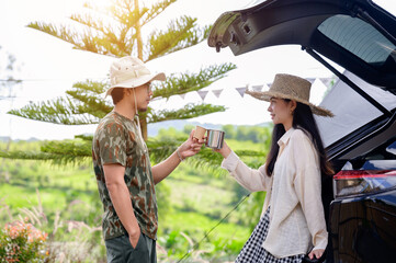 Asian female tourists and man talking and drinking coffee happily in the back of an SUV while camping on vacation with nature scenery in rural travel