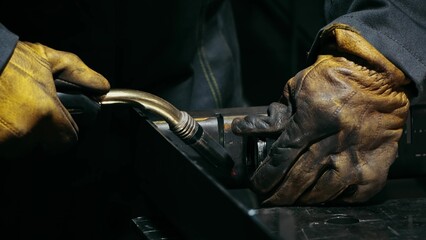 Close-up of a blacksmith welder working with metal using a welding machine, bright sparks and flashes in slow motion