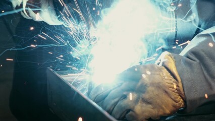 Close-up of a blacksmith welder working with metal using a welding machine, bright sparks and flashes in slow motion