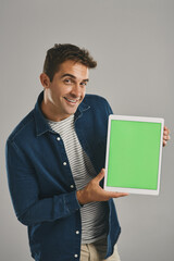 Poster - Green screen, portrait and tablet with man in studio isolated on gray background for advertising or marketing. App, display and smile with happy user in casual outfit for notification or promotion