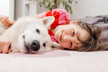 Teenage girl lying with dog on floor, hugging and spending time together. Pet care concept